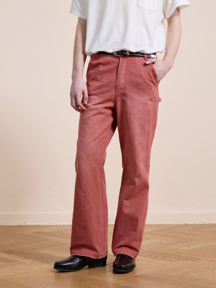 A person stands indoors on a wooden floor wearing a white T-shirt, FOUND Canvas Faded Pants with a belt, and black shoes, with one hand in their pocket.