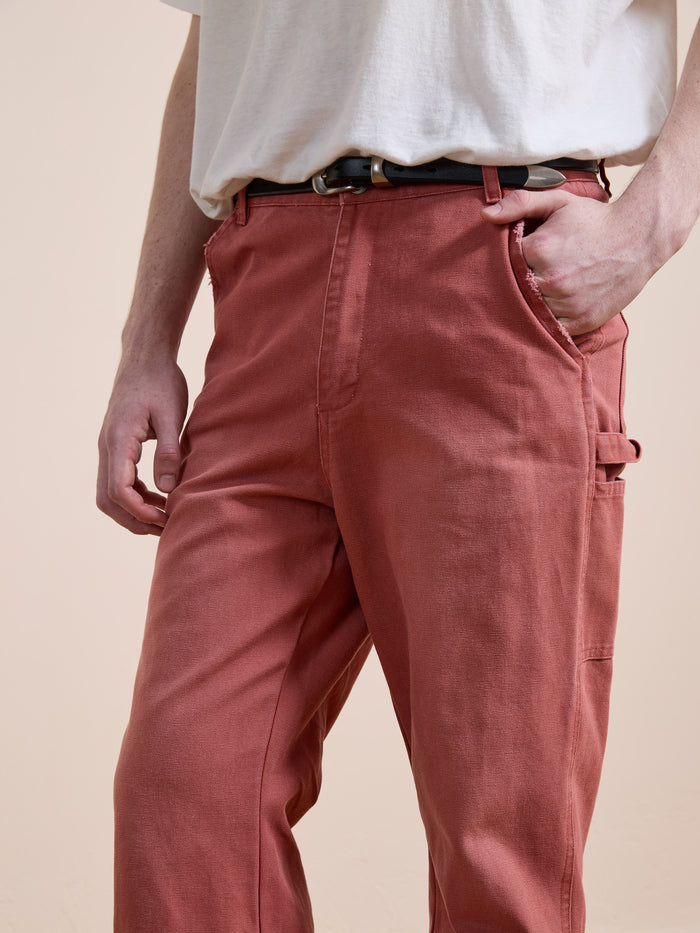Model wears FOUND’s Canvas Faded Pants in vintage salmon wash—high-waisted, loose-fitting style—paired with a white t-shirt and black belt, hand in pocket, against a plain background.